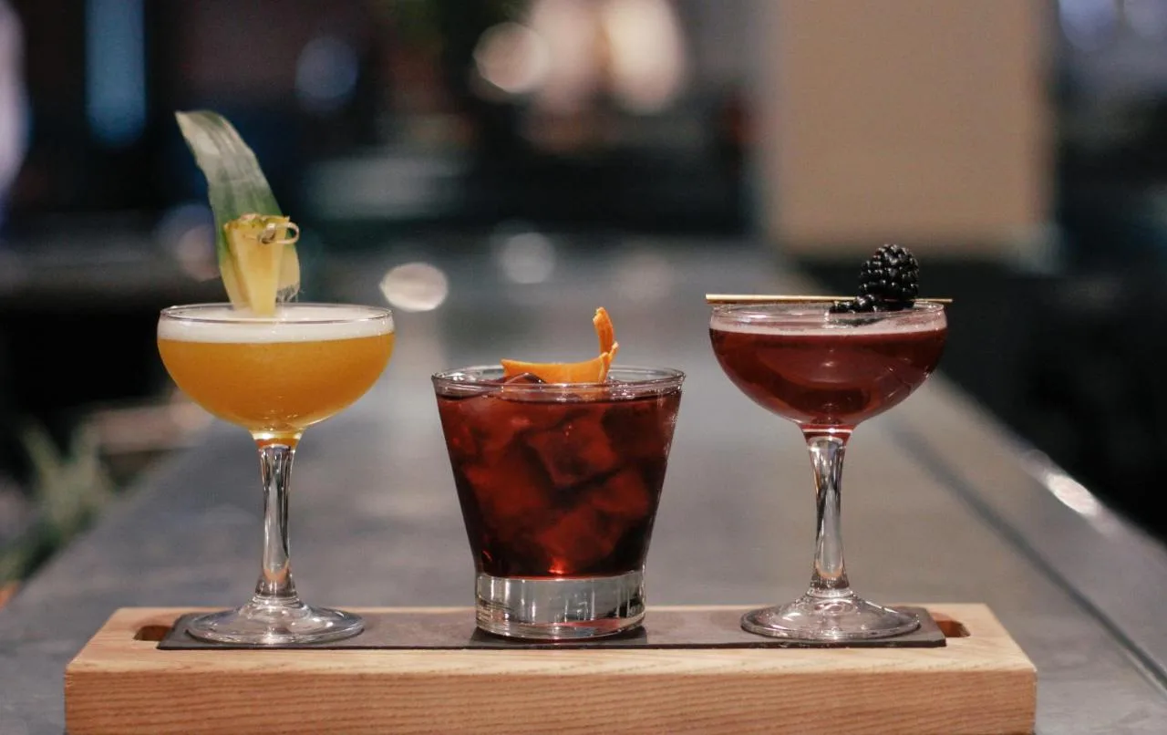 three different cocktails sitting on a wooden tray at The Mandeville Hotel in London